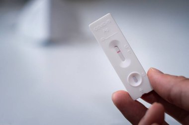 Hızlı bir covid-19 testi tutan bir elin seçici odak noktası beyaz bir tabloda negatif sonuç verir.