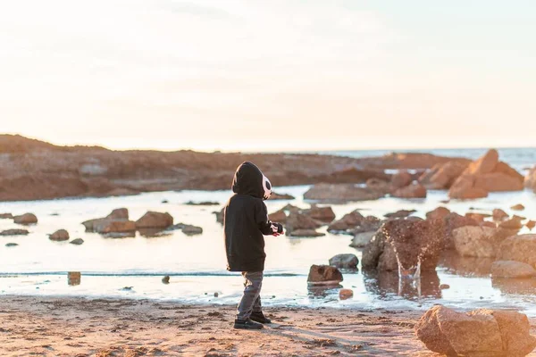 日落时男孩站在岩石河畔的背景图 — 图库照片
