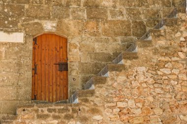 İspanya 'nın Denia kentindeki taş bir duvarda eski ahşap bir kapının önündeki merdiven manzarası.
