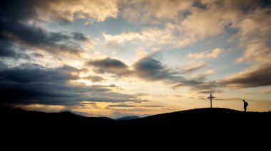 Tirol 'da gün batımında haça ulaşan bir yürüyüşçünün güzel bir görüntüsü.