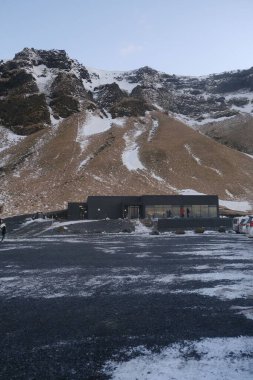 Reynisfjara sahilinde karlı dağlarla çevrili bir binanın dikey görüntüsü.