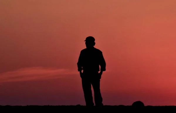 ポケットに手を入れて夕日の空に向かって立っている男のシルエット — ストック写真