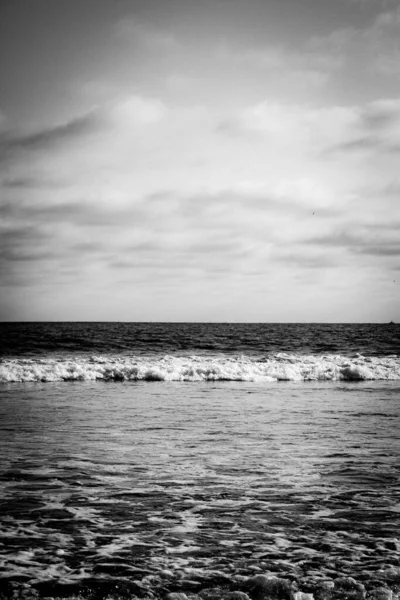 Pionowe Czarno Białe Ujęcie Piankowych Fal Morza Pod Chmurnym Niebem — Zdjęcie stockowe