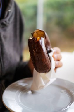 Çikolatalı çörek tutan bir elin dikey görüntüsü.