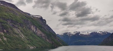 Norveç, Sunnmore 'da bulutlu gökyüzünün altında Geirangerfjord ve Akerneset dağlarının manzarası