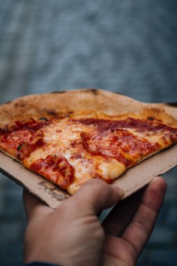 Elinde bir dilim pizza tutan bir erkeğin dikey görüntüsü.