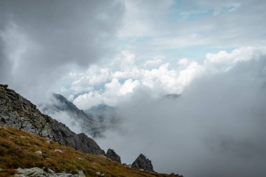 Bulutlu gökyüzünün altında kayalık tepeleri olan büyük dağlardan oluşan güzel bir manzara.