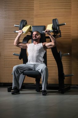 Güzel bir kas geliştirme vücut geliştiricisi, spor salonunda kablolu TV ile omuz ve ağırlık egzersizi yapıyor.