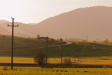 Etrafında elektrik hatları ve istasyonlar olan tarlalar, arkada sisli dağlar ve gökyüzü.