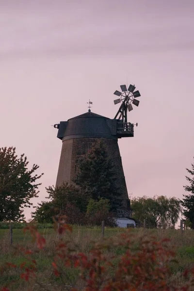 A vertical shot of an old windmill in a field in the countryside at sunset