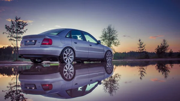 Egy Audi Annak Tükröződése Nedves Úton Naplementekor Hátulról Nézve — Stock Fotó