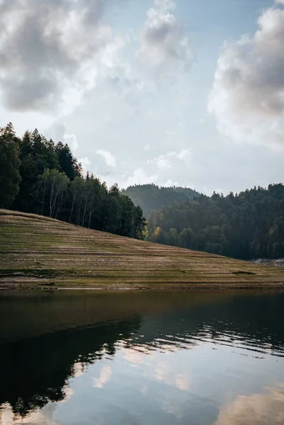 青い空の下 濃い緑の山の森に囲まれた湖の風景 — ストック写真