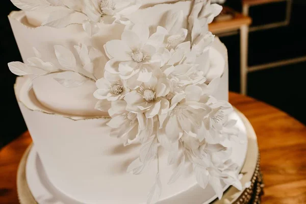 在木制桌子上的白色大结婚蛋糕上放着一束白花的特写 — 图库照片