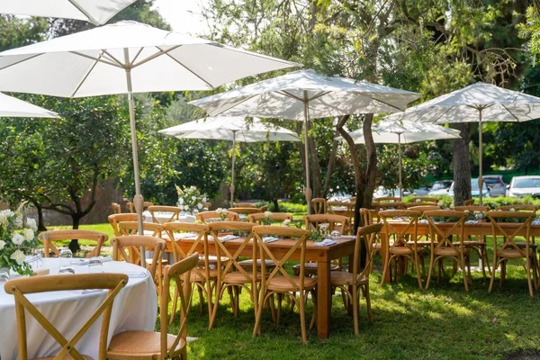 stock image The tables under the white parasols decorated with delicate bouquets prepared for the wedding ceremony