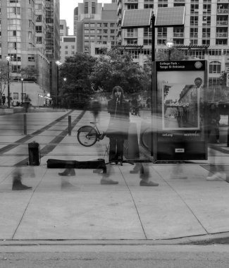 Dikey gri tonda genç bir kadın Toronto, Kanada 'dan geçen insanlarla sokakta şarkı söylüyor.