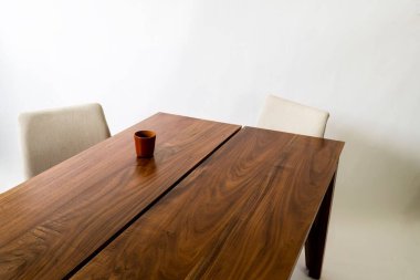 Tahta bir masa, iki sandalye ve bir fincan, beyaz bir arka plana karşı masaya yerleştirilmiş.