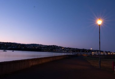 Shaldon Devon 'daki mor gökyüzüne karşı nehir kıyısında parlayan aydınlık bir sokak feneri.