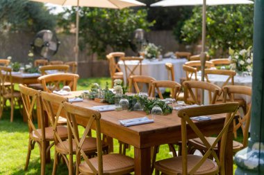 Beyaz şemsiyelerin altındaki masalar düğün töreni için hazırlanmış narin buketlerle süslenmiş.