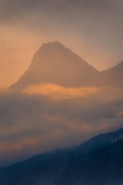 Gün batımında bulutların içindeki dağın tepesinin bir görüntüsü..