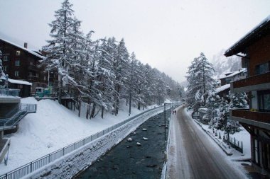 Karla kaplı çam ağaçları ve İsviçre 'nin Interlaken kentindeki apartmanlarla çevrili donmuş bir nehirle güzel bir kış manzarası.