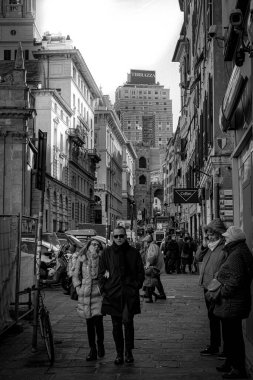 Roma, İtalya 'dan geçenlerin geçtiği dar bir caddenin dikey gri tonlu görüntüsü.
