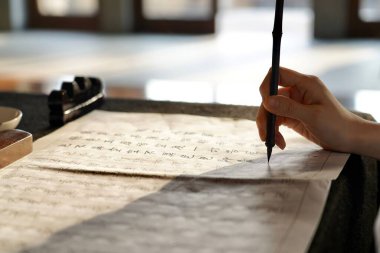 Kağıtların üzerinde geleneksel bir Çin fırçası tutan bir kişinin sığ bir odak noktası.