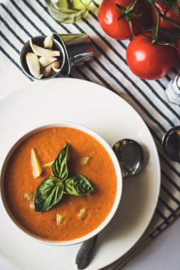 Yuvarlak beyaz bir kasede fesleğen yapraklarıyla süslenmiş domates çorbasının dikey görüntüsü.