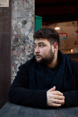 Masaya yaslanmış ve yüzünü çevirmiş beyaz bir adamın dikey görüntüsü.