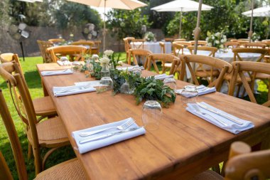 Beyaz şemsiyelerin altındaki masalar düğün töreni için hazırlanmış narin buketlerle süslenmiş.