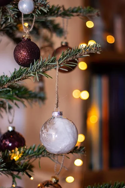 一个垂直的圣诞球特写挂在云杉针上 背景上有吊灯 — 图库照片