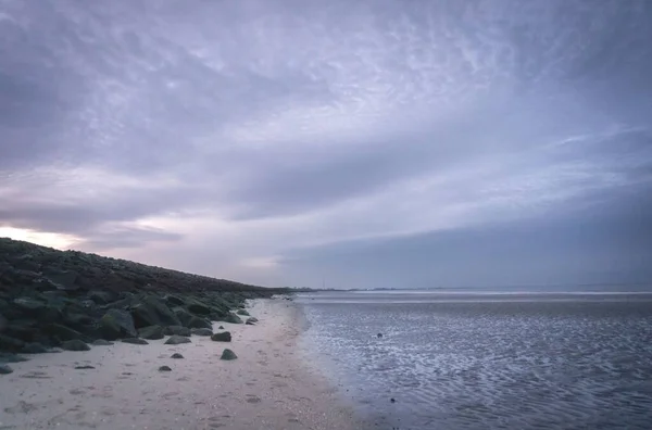 夕暮れ時に黒い岩で満たされたビーチで海岸を満たす海の景色 — ストック写真