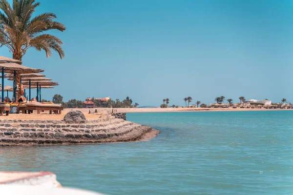 那人躺在苏尔坦湾El Gouna海滩 手里拿着草伞和棕榈 — 图库照片