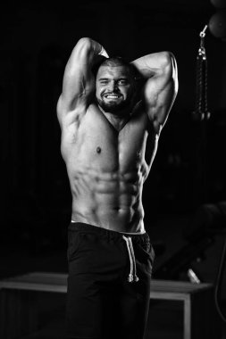 Spor salonunda poz veren ve kaslarını esneten sağlıklı beyaz bir adamın dikey gri tonda çekimi.