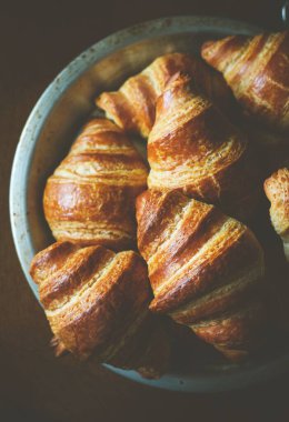 Siyah arka planda bir kasede taze yapılmış Fransız kruvasanlarının dikey üst görüntüsü.