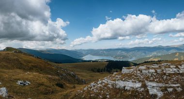 Tepelerde yemyeşil ormanlarla çevrili bir göl manzarası.