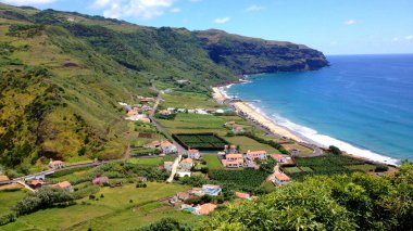 Portekiz, Azores 'te güneşli bir günde mavi okyanus manzarası ve dağların altındaki evler.
