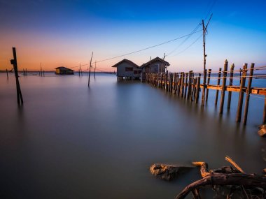 Tayland 'daki Songkhla Gölü' ndeki tahta kutupların üzerinde parlak bir günbatımı manzarası.