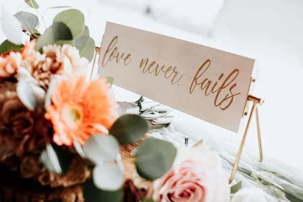 A decorative LOVE NEVER FAILS sign on a wedding taable with afloral centerpiece