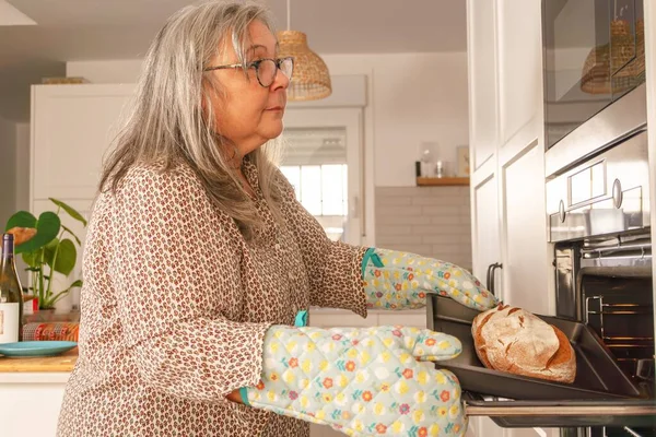 Starší Bělovlasá Žena Dává Chléb Trouby Kuchyni Doma — Stock fotografie