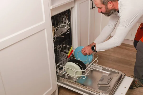 Muž Bílém Tričku Dává Nádobí Myčky Kuchyni Svého Domu — Stock fotografie