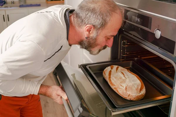 Sakallı yaşlı adam evinin fırınına ekmek koyuyor.