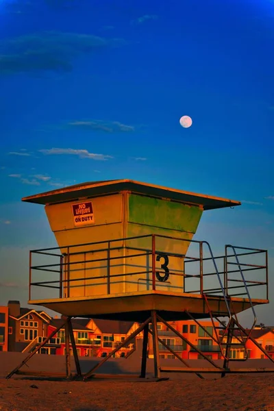 背景に満月と日没の間にビーチのライフガードタワーの垂直方向 — ストック写真