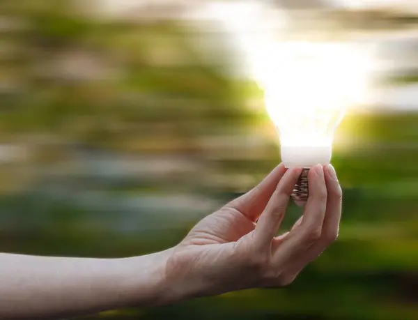Крупный План Женской Руки Держащей Светящуюся Лампочку Размытом Зеленом Фоне — стоковое фото