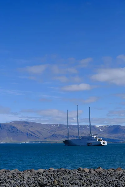 在冰岛山脉前的蓝色海面上的一艘帆船的垂直镜头 — 图库照片