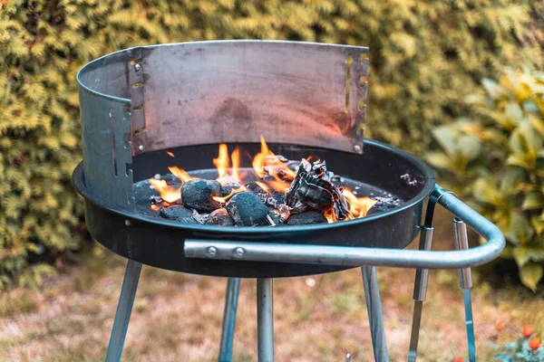 stock image A barbeque grill with little flames placed in a garden, with charred potatoes on it