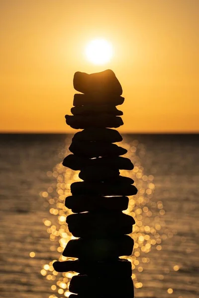 日没時に太陽と輝く青い海に対して積み上げられた石の垂直接近ショット — ストック写真