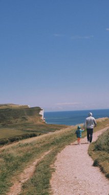 Bir erkek ve bir çocuğun Beachy Head uçurumuna ve Sussex, İngiltere 'deki deniz fenerine giden patikada yürüdüğü dikey bir çekim.