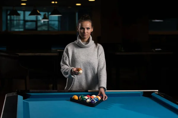 stock image A young woman standing at the pool table arranging billiard balls in a triangle.