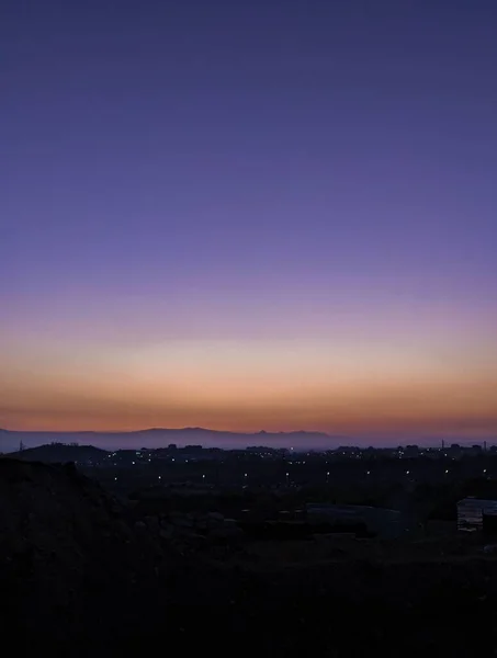 背景に丘がある町の上の美しい夕日の垂直ショット — ストック写真
