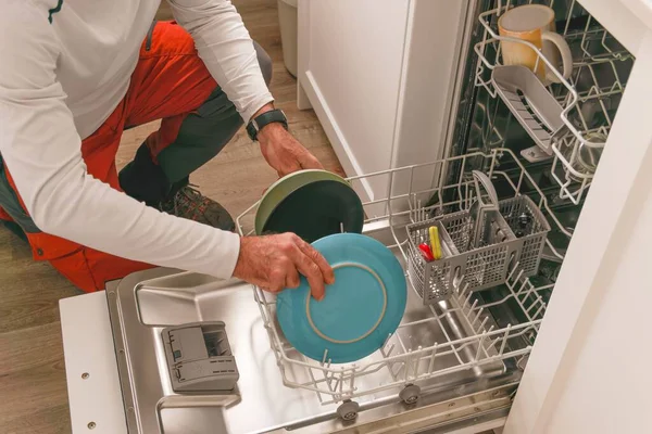 穿着白色T恤的男人把碗碟放在洗碗机里 放在厨房里 — 图库照片